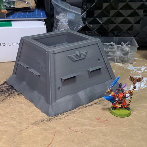 A grey plastic model sci-fi bunker next to a brightly painted space wizard on a messy desk.