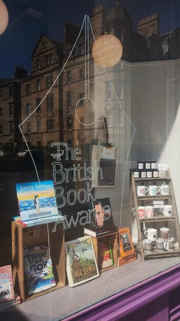 Outside view of the finished British Book Awards window with winning books, and the pen nib logo painted on the glass, close up