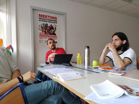 Des militants et public discutant et s’écoutant autour d’un ilôt de table. On voit des exemplaires du manifeste et des notes papiers.