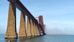 Forth Bridge viewed from the shore near the southern end.&nbsp; Stone pillars march across the water towards the famous cantilever sections.&nbsp; The second cantilever is partially obscured by haar, the rest of the bridge and the Fife coast are completely obscured by the mist.