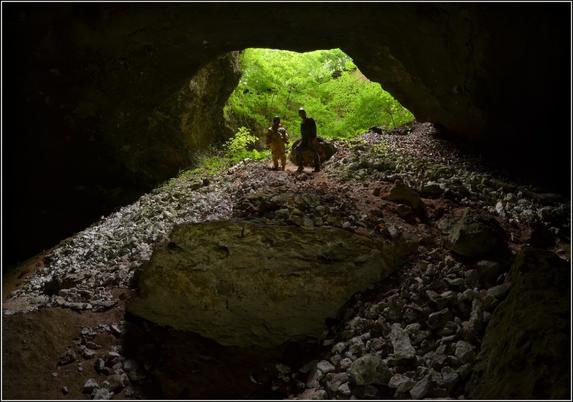 Deux personnes en souterrain. Au porche de la cavité l'on aperçoit une forêt.