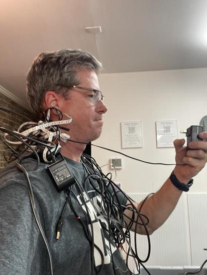Picture of me from the side with a large tangle of cables draped around my shoulders. Staring at a power plug brick while saying “Back Beasts!”