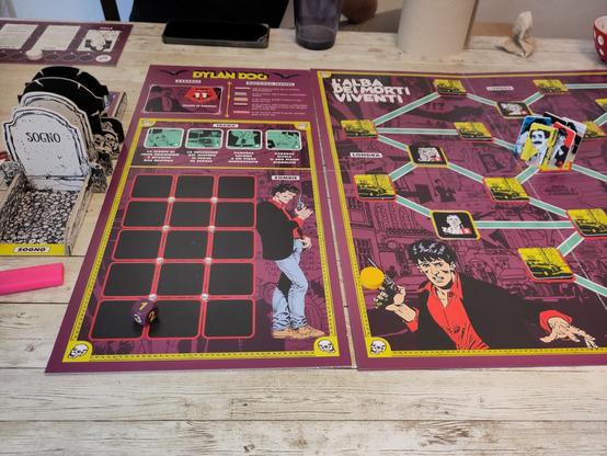 Parziale vista della plancia del gioco da tavolo di Dylan Dog. Al centro della mappa si vedono le pedine dei personaggi tra cui spiccano i segnalini di Groucho, in giallo, e Dylan stesso in rosso. A sinistra si vede un portacarte a forma di tomba dove, sulla lapide bianca, si legge "Sogno".