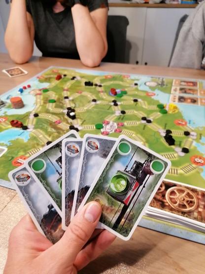 Ich halte Spielkarten des Spieles Switch and Signal in der Hand. Dahinter ist das Spielbrett zu sehen.