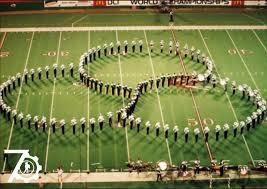 A drum corps forms connecting rings on a football field, showcasing a large circle pattern created by the musicians in uniform.