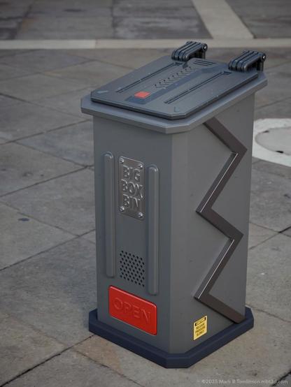 Tall grey waste bin with a zig-zag support bar on the side. A metal plate inscribed with "Big Box Bin" a foot opener in red with open on on it.