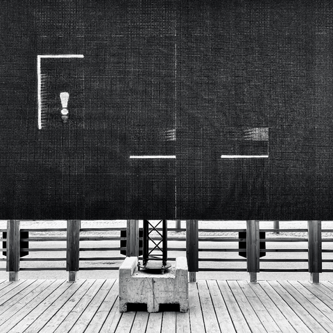 The black mesh of a big screen on the edge of a beer garden shows an exclamation mark and some lines, while partially concealing a walkway.