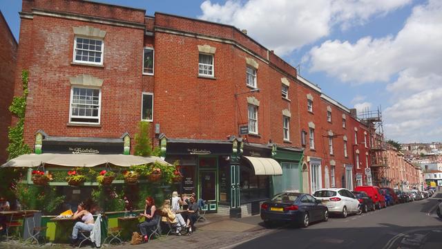 A pub, with patrons sitting outside, with a long, brick terrace off to the right.