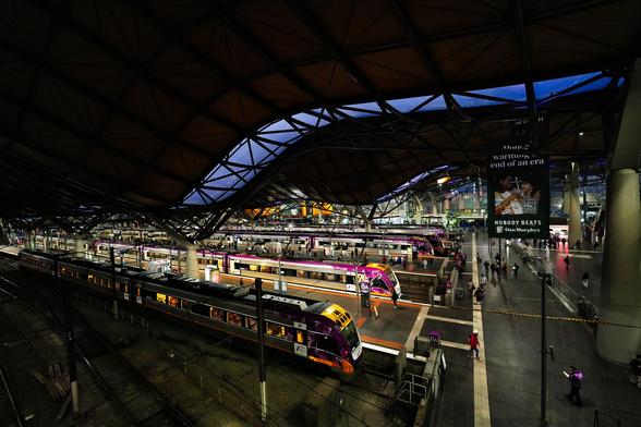 Southern Cross Station, formerly known as Spencer Street Station, is a major railway hub located in Docklands, Melbourne. Opened in 1859, it was renamed in 2005 following a significant redevelopment. The station is renowned for its distinctive undulating roof, designed by Grimshaw Architects in collaboration with Jackson Architecture, which spans an entire city block and facilitates natural ventilation, reflecting sustainable architectural principles. Serving as the terminus for Victoria's regional V/Line services, as well as interstate trains to Sydney and Adelaide, Southern Cross also connects with Melbourne's metropolitan rail network and the City Loop. The station features 16 platforms and two main concourses at Bourke and Collins Streets, accommodating over 170,000 daily commuters. Despite its modern design and functionality, the station has faced criticism over maintenance issues, including malfunctioning escalators and air quality concerns due to diesel emissions from idling trains. Nevertheless, Southern Cross Station remains a vital component of Melbourne's transportation infrastructure, symbolizing the city's blend of historical significance and contemporary urban development.