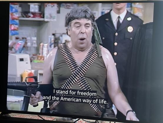 Man with ammo belts strapped over chest and automatic rifle in hand saying “I stand for freedom and the American way of life.”