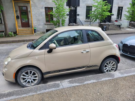 A small beige car, parked in Montréal.  There appears to be a monkey in the car, but it is sitting in the passenger seat.
