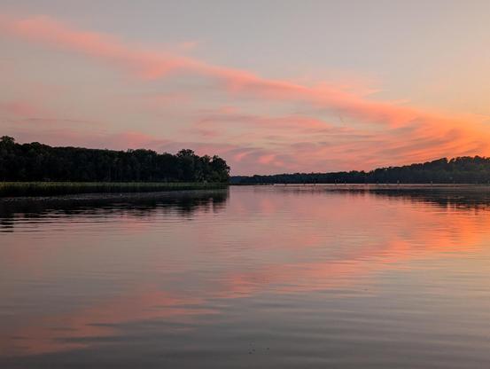 Pink clouds in a large horizontal v shape reflect in Mattawoman Creek and stretch over a bend in the shoreline