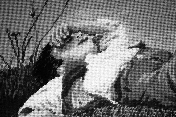 Close-up shot of needle work. A young boy rests on a hill his hand covers his eyes.