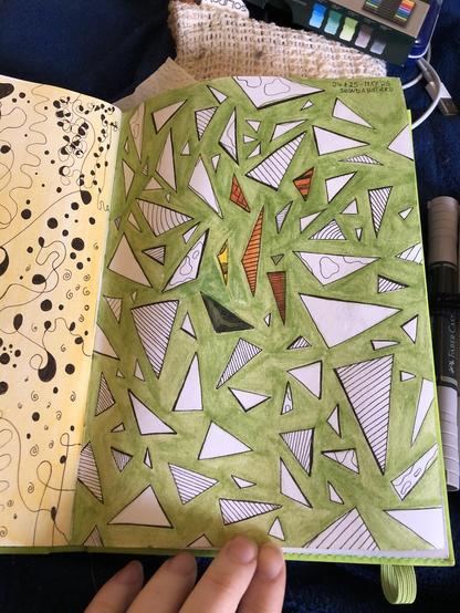 This is a photo of sketch book page. The background colour is unevenly brushed with watercolour in a fresh grass green tone. Scattered across the page are triangles in various sizes. Some have patterns made of lines or waves. In the centre of the page, a few triangles are coloured in yellow, orange and a very dark green.