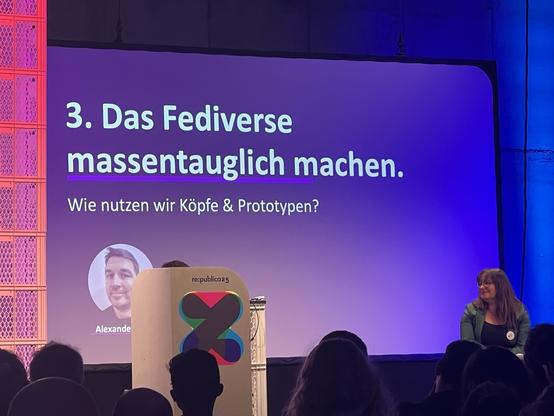 Man sieht die Bühne von Stage 7, vorne rechts sitzt Pia Marie Lexa vom Media Lab Bayern. Im Hintergrund sieht man eine Präsentation mit dem Text "3. Das Fediverse massentauglich machen. Wie nutzen wir Köpfe & Prototypen?"