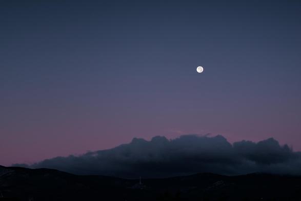 Fotografia de un valle nocturno en la q se ve un degradado en el cielo de azul a morado la luna lena en la parte superior derecha y en el tercio inferior se aprecia el valle bajo una gran nube gris