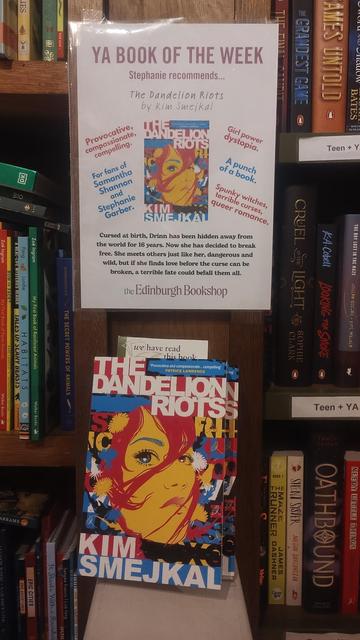 A copy of The Dandelion Riots on a shelf in the Edinburgh Bookshop, in front of a poster declaring it "YA Book of the Week"