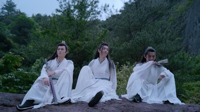 Seated in row side by side on a rocky prominence in the Cloud Recesses back hill are teens Jiang Cheng, Wei Wuxian, and Nie Huaisang, in assorted variants of casual sprawl. Jiang Cheng is resting his left elbow in his left knee, Sandu in its sheath in his left hand, and his right forearm draped over his right knee at a lower left than the left due to his right leg being further extended. Wei Wuxian is leaning back on his hands, right knee pulled up and left leg fully extended, head turned in Huaisang's direction. Huaisang has both knees pulled up close to his torso but with his legs set wide, elbows resting on his knees and right wrist held in front of his laughing mouth. A mostly closed paper folding fan is held in his right hand.
