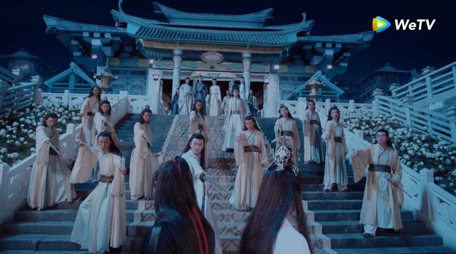 On the Koi Tower steps, perspective up the steps from behind Wei Wuxian and Lan Wangji. Wuxian and Wangji stand close together, back to back, both with heads turned to look up at the Jin disciples arrayed on the steps above them and beyond to where Guangyao stands at the top in line with Nie Huaisang and Jiang Cheng to his right and Lan Xichen to his left at some distance.