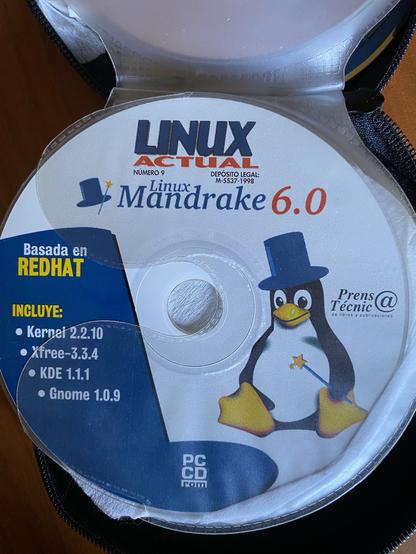 Un CD de la revista Linux Actual con la imagen de Mandrake 6.0. El disco viene ilustrado con un dibujo de Tux (el pingüino mascota de Linux) disfrazado de mago con varita y chistera