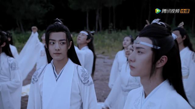 Wei Wuxian looks over a Lan Wangji with a small smile while Wangji is looking up toward the sky. They are surrounded by other disciples gesturing towards and watching the released sky lanterns float away.