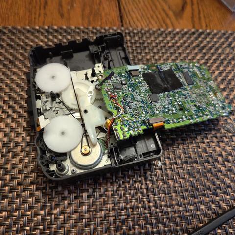 The Sony Walkman WM-FX455 opened up with the circuit board removed but still attached with one wire. With it out of the way, the gears and flywheels of the player are visible and the original band is still installed. I removed the belt and replaced it for the repair.