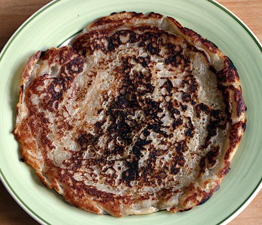 Pancake made of 200g discarded sourdough starter thinned with 75g milk (this made 2). showing bubbles from the ferment and many shades of dark brown, golden brown, cream etc from the cooking.  Thick, think more galette than crêpe.
