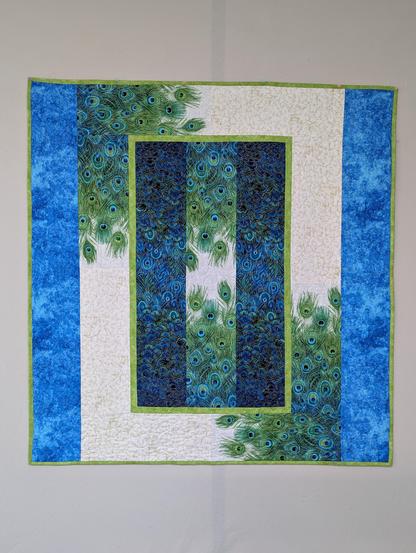 a finished quilt, with blue and green peacock feather print, lime green print narrow inner border and binding, and bright blue print borders on the sides.