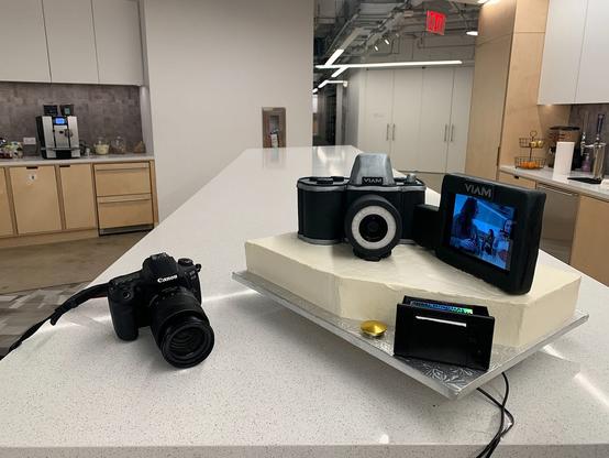 A photo of a canon camera, next to the interactive cake that has a camera on it as well as a display, button and a thermal printer