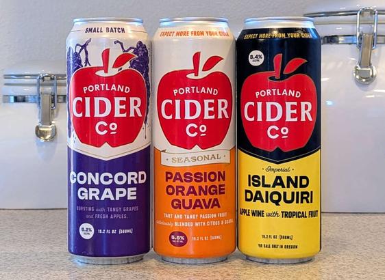 Three cans of specialty hard cider from Portland Cider Company: Concord Grape, Passion Orange Guava, and Island Daiquiri
