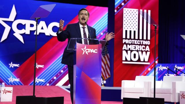 Mike Lindell speaks on stage at the Conservative Political Action Conference, flanked by signs that say "CPAC" and "Protecting American now."