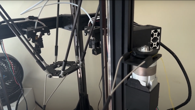 The frame of a delta 3D printer is shown. The toolhead of the 3D printer does not have a hotend installed, but instead has a frame with a circular hole in the middle. The frame of a delta 3D printer is shown. The toolhead of the 3D printer does not have a hotend installed, but instead has a frame with a circular hole in the middle.
