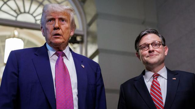 Trump and Mike Johnson standing next to each other in a white marble hallway while wearing blue suits.