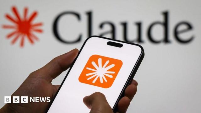 A close up of a hand holding a smartphone displaying Anthropic's Claude logo on a white screen. The logo is displayed in the background of the image behind it.