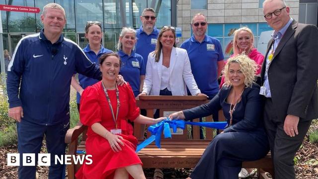Hospital staff - some standing- wearing their blue uniformed T-shirts- with two executive members - one woman in red dress and the other in a blue suit- cutting a blue ribbon with Micky Hazard in a jogging set standing beside the woman in red dress