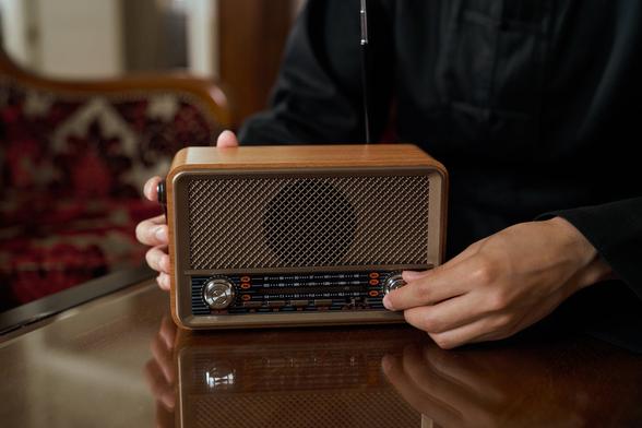 fotografía de una radio de estilo antiguo con unas manos en los diales del aparato sintonizando