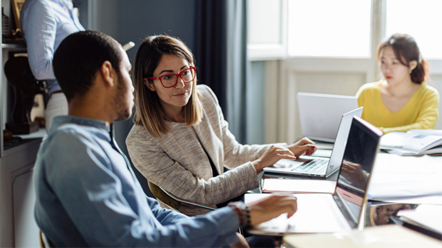 Three people sit around a desk working on laptops