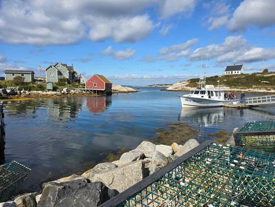 A serene scenery from Peggy's Cove, with a small bay with wooden houses on the shore, a lobster trap, and a white small boat.