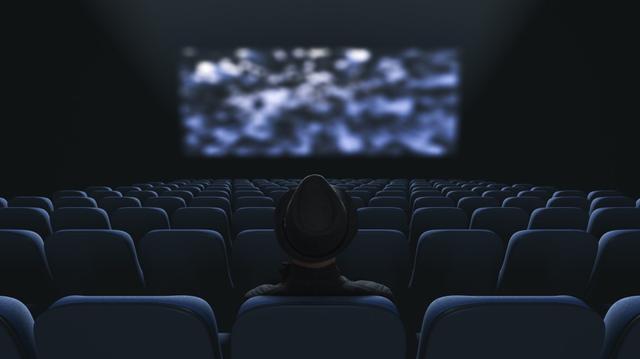 A picture of a person watching a screen in an empty movie theater.
