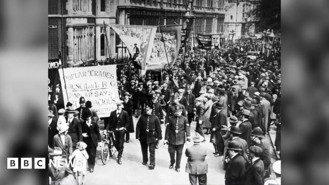 Black and white photograph dating from 1925 showing march, fronted by a group of policemen wearing the uniform of the time. The marchers, mostly men, are carrying banners and there are crowds of people lining the street on either side.