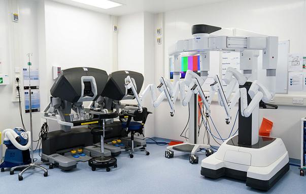Image of a room in a hospital featuring two surgical robots and two control systems.