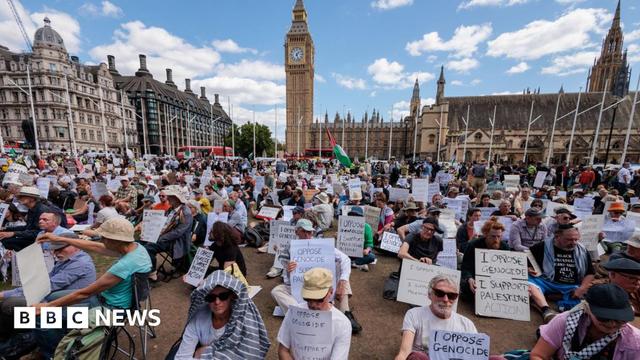 Hundreds of people hold signs reading 'I Oppose Genocide - I Support Palestine Action' while sitting in Parliament Square. Big Ben's clocktower is seen in the background as well as the Palace of Westminster. Hundreds of people hold signs reading 'I Oppose Genocide - I Support Palestine Action' while sitting in Parliament Square. Big Ben's clocktower is seen in the background as well as the Palace of Westminster.