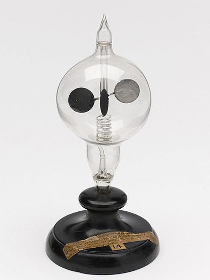 Image of a wooden stand holding a sealed glass bulb with a spinning set of vanes, each of which has a lit and dark side.
