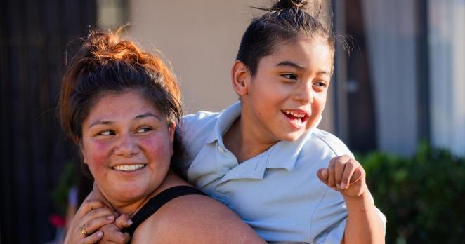 Tustin, CA - September 16: Cassandra Gonzalez carries her nephew Elijah Maldonado while playing tag with other family members outside her home on Tuesday, Sept. 16, 2025 in Tustin, CA. (Juliana Yamada / Los Angeles Times)