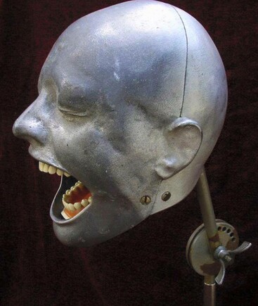 A metal head with its mouth wide open to make it look like it is screaming. There is a set of artificial teeth inside the mouth.