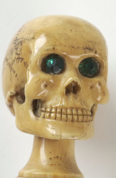 A skull atop a long cane with striking green eyes made from glass