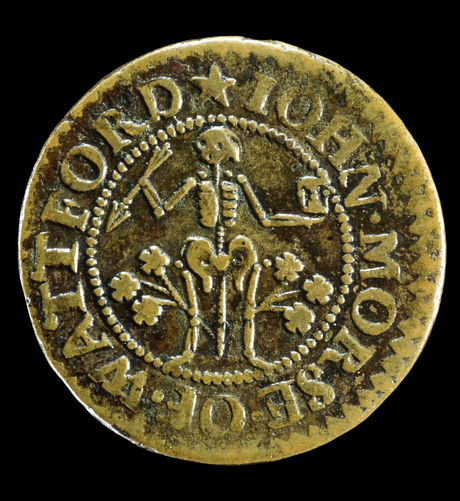 A skeleton holding a dart and an hourglass in the middle of a round token encircled by text.