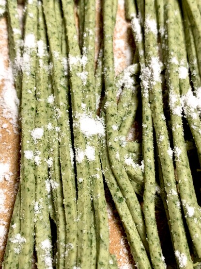 A close up image of the green moringa soba noodles before boiling. The are light green with flecks of dark green. White flour is dusted on top to keep them from sticking. 
