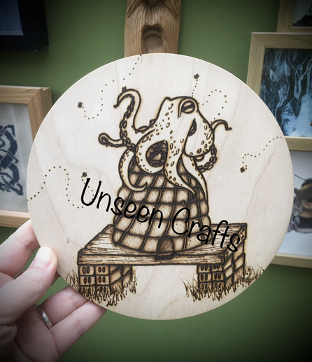 Circular wooden plaque with a hand burned design. An octopus sits atop a mound shaped beehive. The hive sits on a piece of wood which sits on bricks. There are multiple bees flying around and one sitting on an octopus limb.