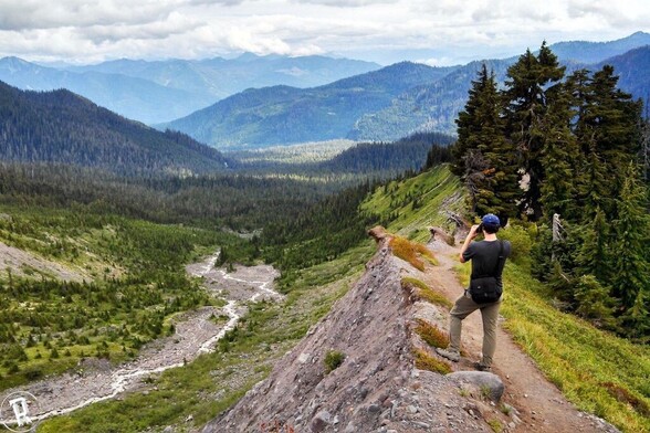 Man on rocky trail looking across valley with binoculars at Mt. Baker-Snoqualmie National Forest.